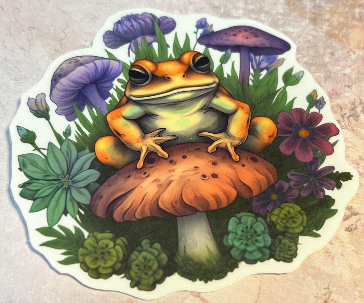 Tangerine color Frog atop a rust colored mushroom with greenery and flowers surrounding the image and a few purple mushrooms in the background (etsy image id: 6694260741)