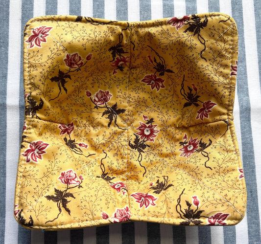 Shows the top side of a golden yellow cotton print bowl cozy for holding your hot soup bowl. it has a small vine print with reddish pink flowers. (etsy image id: 6723713808)