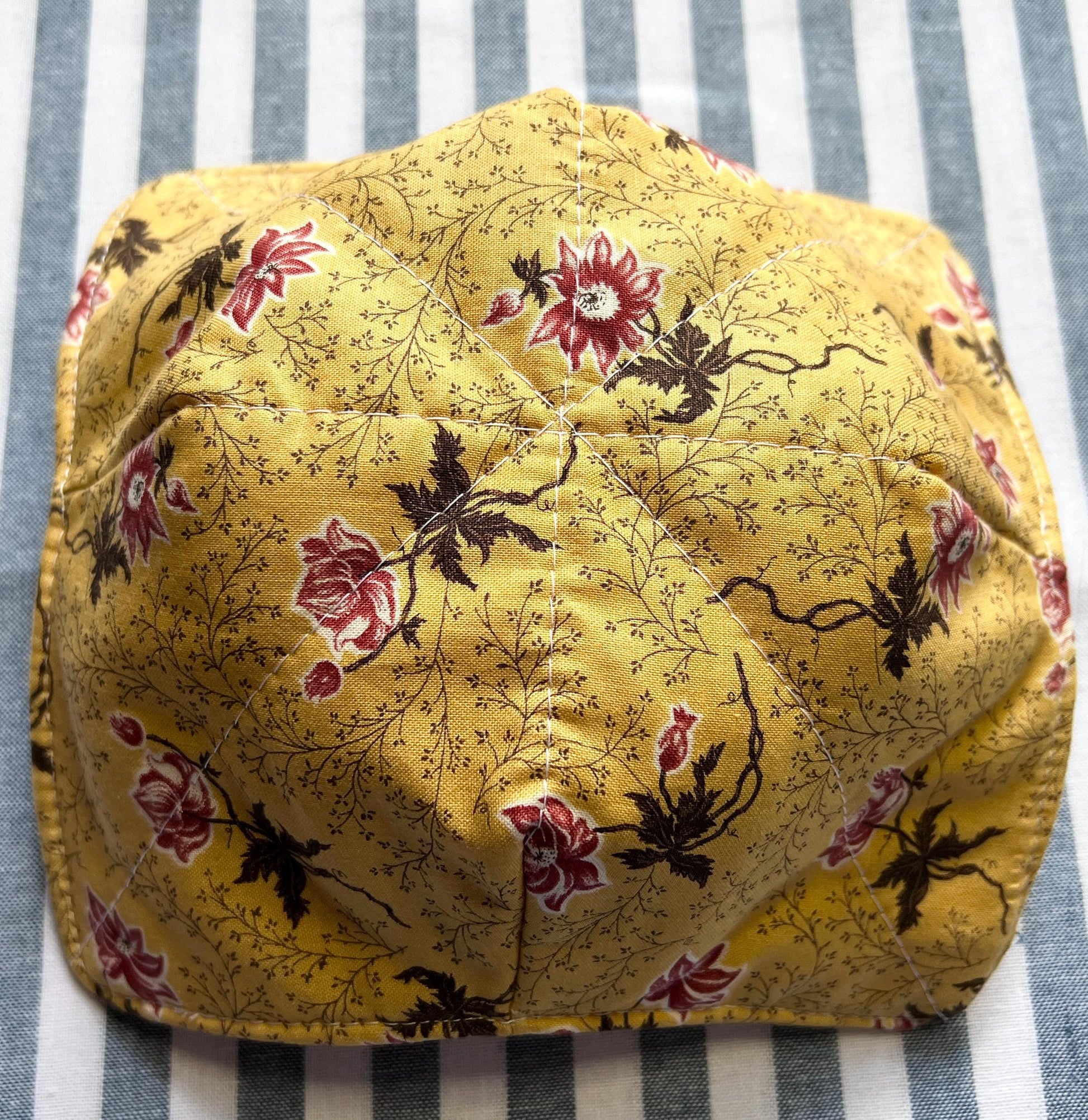 Shows the underside of a golden yellow cotton print bowl cozy for holding your hot soup bowl. it has a small vine print with reddish pink flowers. (etsy image id: 6771741625)