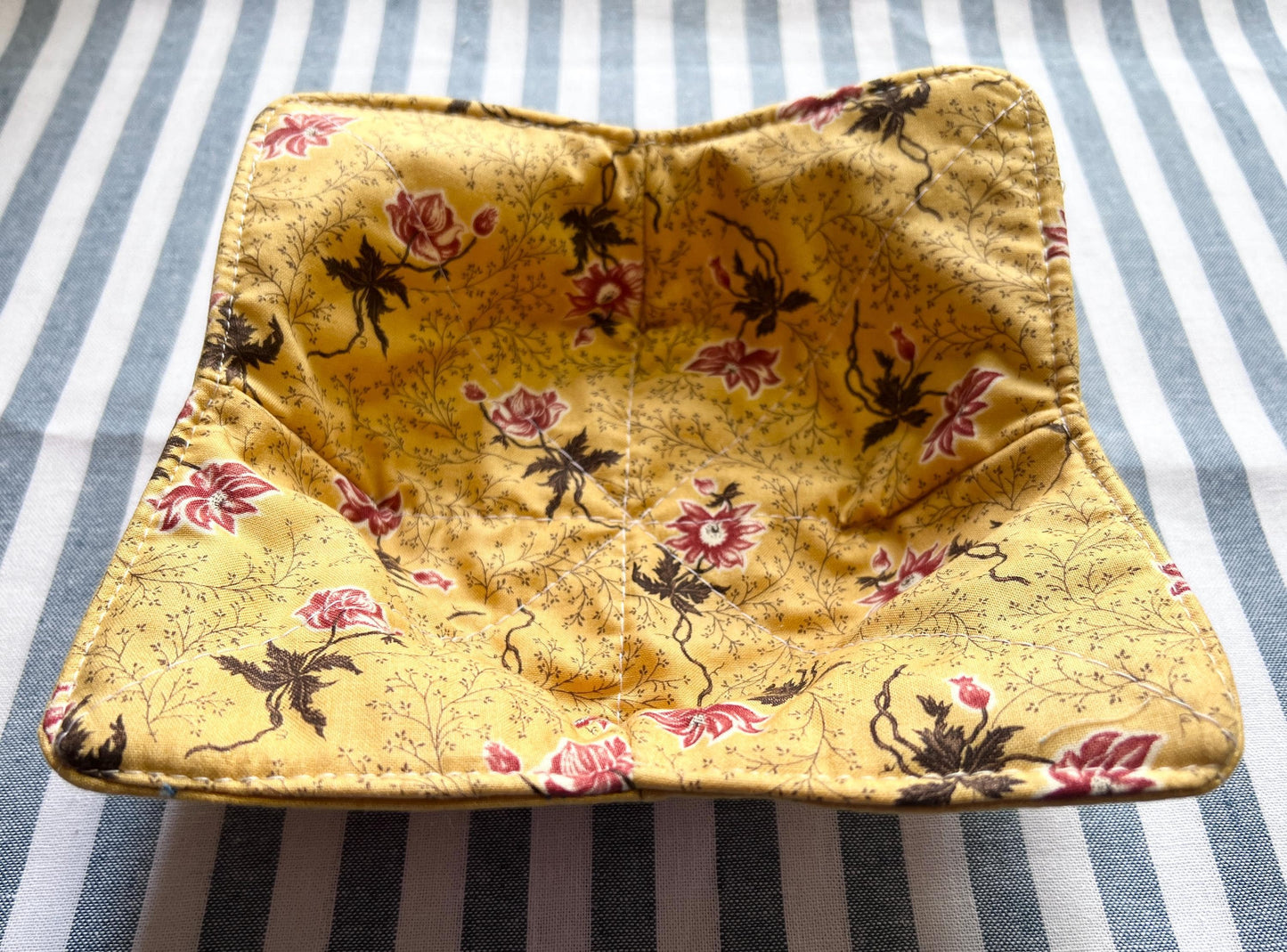Shows the underside of a golden yellow cotton print bowl cozy for holding your hot soup bowl. it has a small vine print with reddish pink flowers. (etsy image id: 6771741917)
